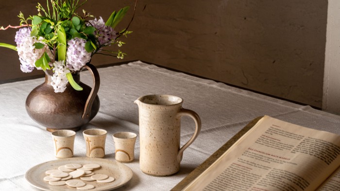 Auf dem Altar stehen Tonteller mit Oblaten und Tonkrug mit drei kleinen Einzelkelchen nebst Bibel und Blumen - alles ist bereit für das Abendmahl.