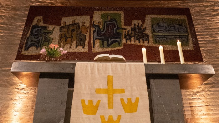 Religiöser Altar mit einem Kreuzmosaik, Kerzen und einem „WTW“-Tuch mit Kronenemblem.