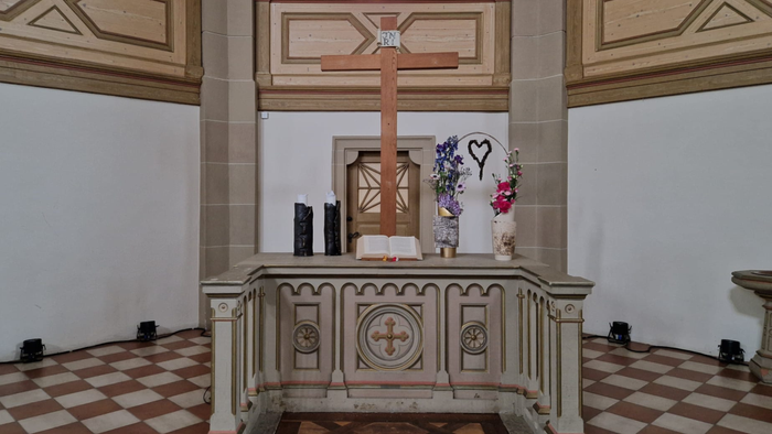 Das Bild zeigt einen Altar in einer Kirche mit Kreuz, Kerzen und Blumen.