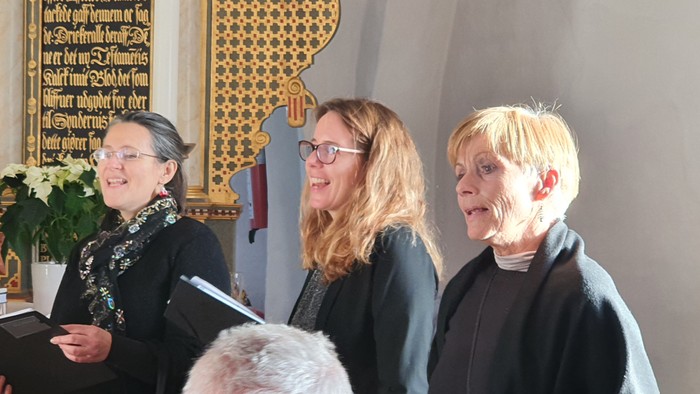 Tre kvinder står sammen og synger i en kirke.