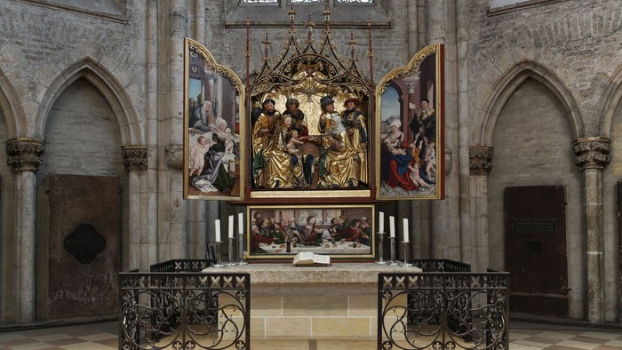 Das Bild zeigt einen Altar in einer gotischen Kirche mit aufwendigen Malereien und einem schmiedeeisernen Zaun.