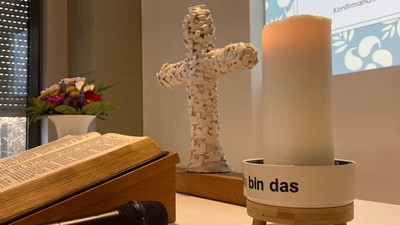 Auf dem Tisch stehen ein Buch, ein Kreuz, eine Kerze und eine Vase mit Blumen