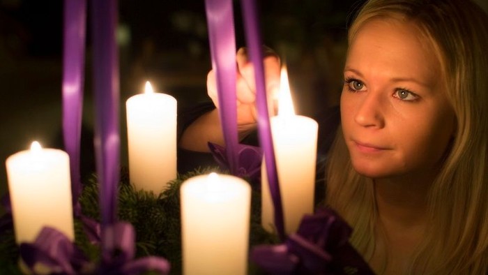 En ung pige med blå øjne holder en adventkrans med lysende lygter.