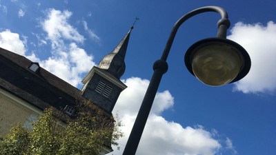 Ein Laternenpfahl vor einer Kirche mit hohem Turm und blauem Himmel.