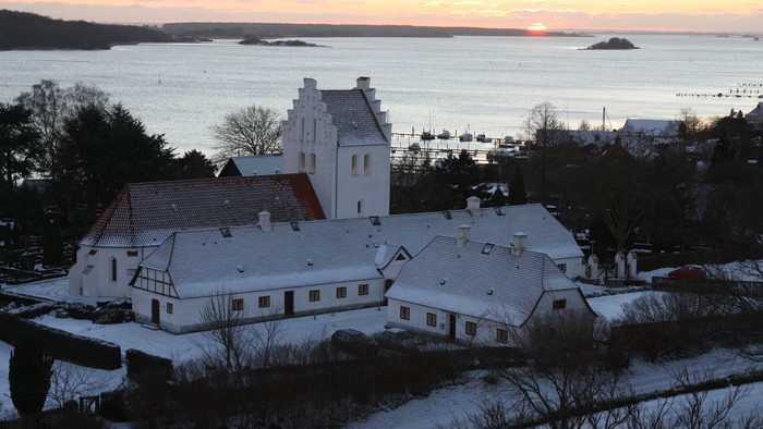 En snede landsby ved havet med en kirke og huse dækket af sne