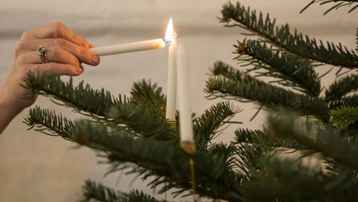 En hånd tænder en lys på en juletree med guldornamenter