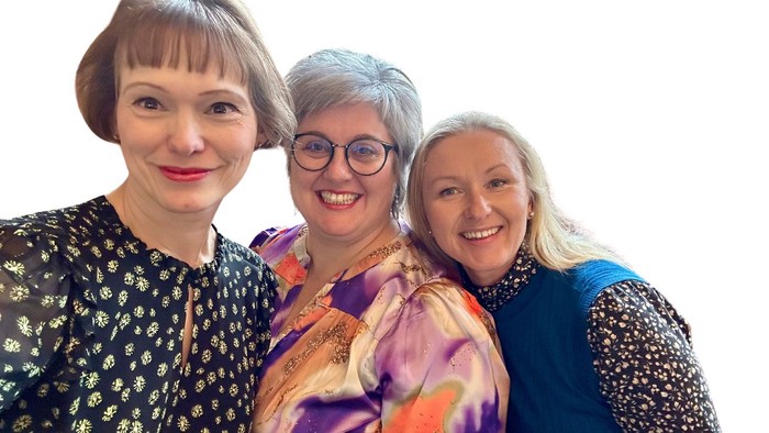Tre kvinder står sammen og smiler til kameraet