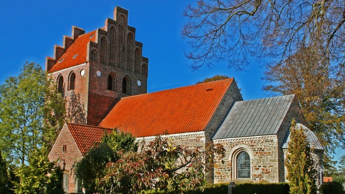 Gammel kirke med røde tag og murstensmureri i solskinn
