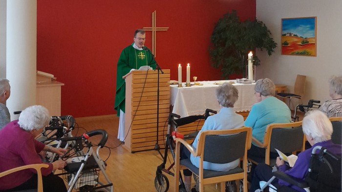 Ein Gottesdienst mit älteren Teilnehmern im Rollstuhl und einem Priester, der die Zeremonie leitet.