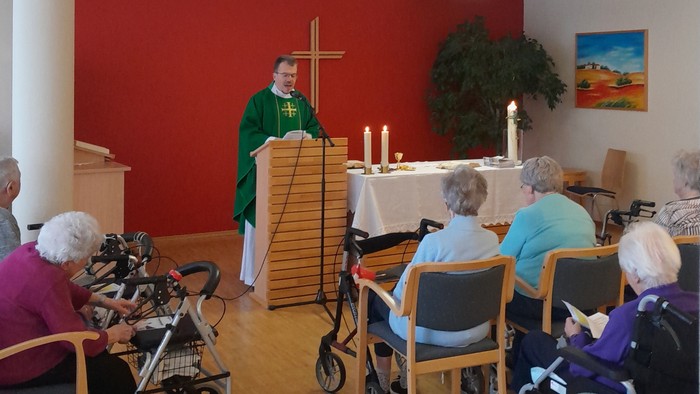 Ein Gottesdienst mit älteren Teilnehmern im Rollstuhl und einem Priester, der die Zeremonie leitet.