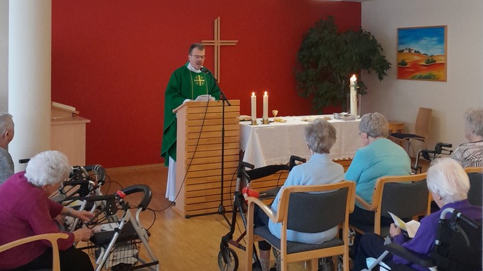 Ein Gottesdienst mit älteren Teilnehmern im Rollstuhl und einem Priester, der die Zeremonie leitet.