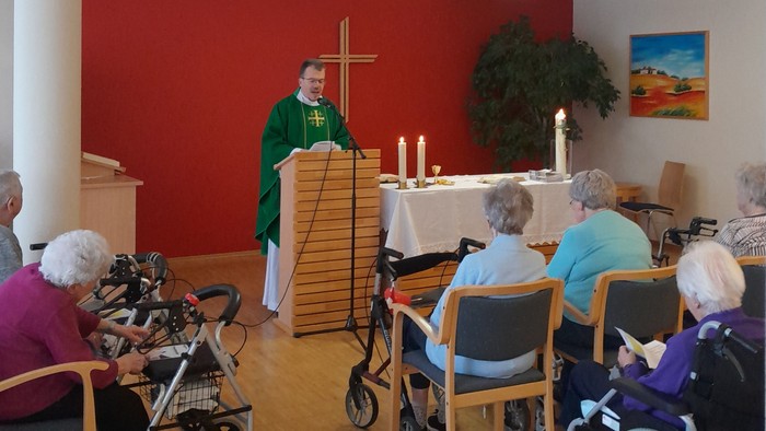 Ein Gottesdienst mit älteren Teilnehmern im Rollstuhl und einem Priester, der die Zeremonie leitet.