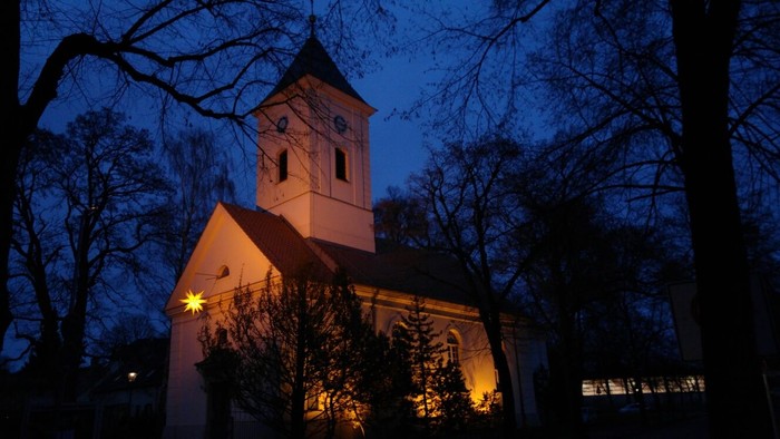 Kirchengebäude bei Nacht, beleuchtet, umgeben von Bäumen