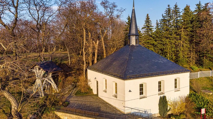 Kleine weiße Kirche mit spitzem Turm in ländlicher Umgebung