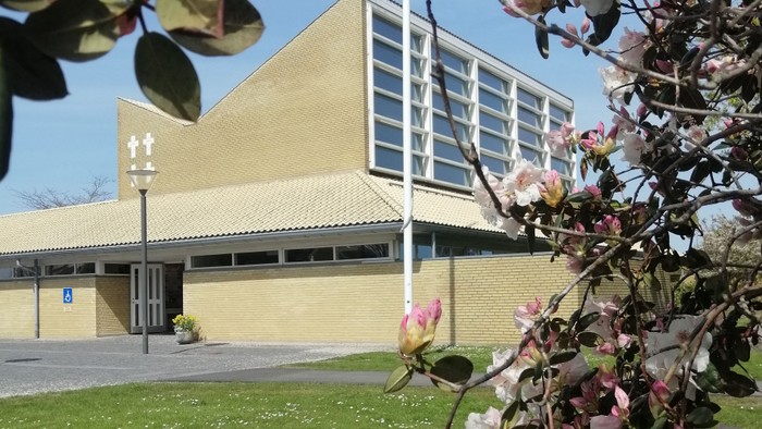 Et gult kirkebygning med blomsterbuske i forgrunden