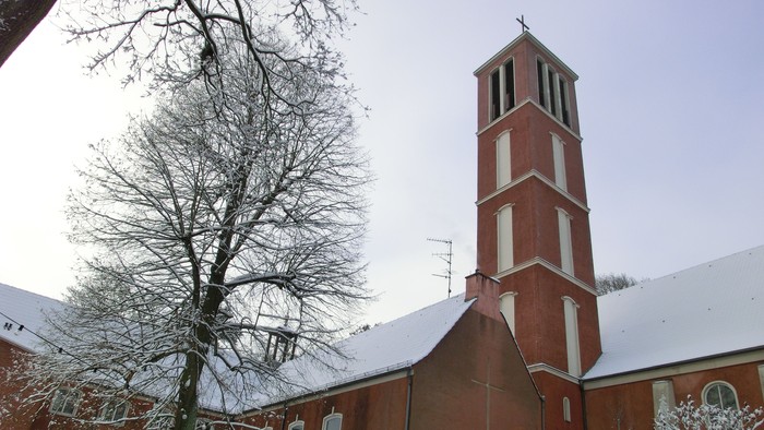 Weiß überzogene Kirche mit hohem Turm und kahlen Baum davor
