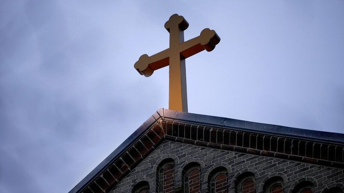 Et gyldent kors på en murstenskirke mod en skyet himmel.