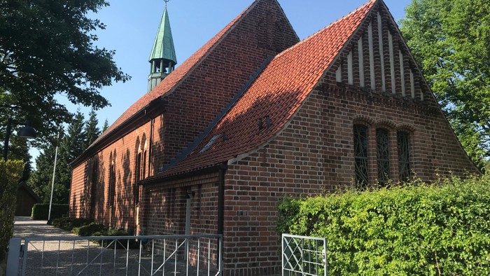 Røde teglkirke med spiret og murstakning.
