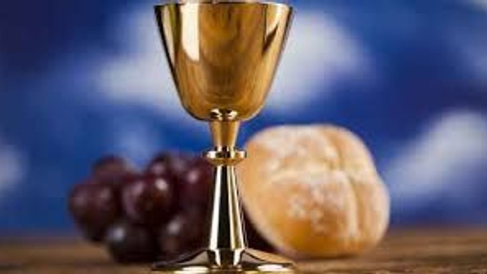 Gyldent bæger med druer og brød på en træoverflade, der symboliserer nadverens elementer.