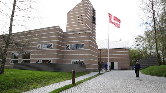 Stor modernist bygning med horisontale linjer og dansk flag på en stang foran.