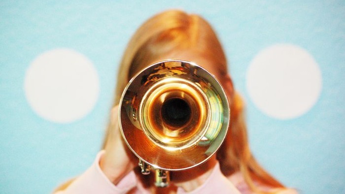 Eine Person spielt eine Posaune vor einem blauen Hintergrund.