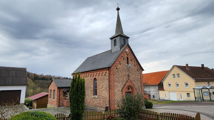 Kirchengemeinde in ländlicher Umgebung mit mehreren Häusern und einem Kirchturm.