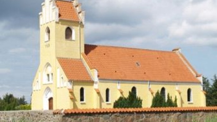 En gul kirke med røde tag og tårn i en grøn og åben landskab