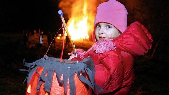 Kleine Mädchen mit Kürbislaterne und pinker Mütze vor Feuer