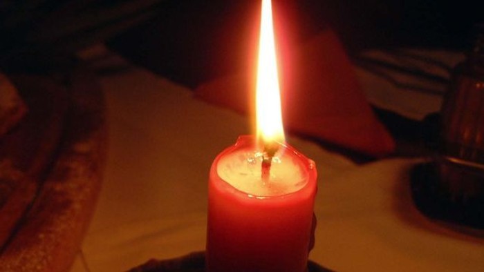 Eine rote Kerze brennt auf einem Tisch.