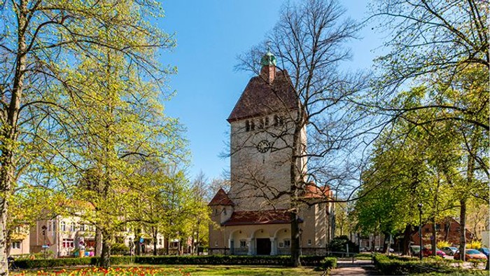 Ein alter Turm steht in einem Park mit Bäumen und Häusern.