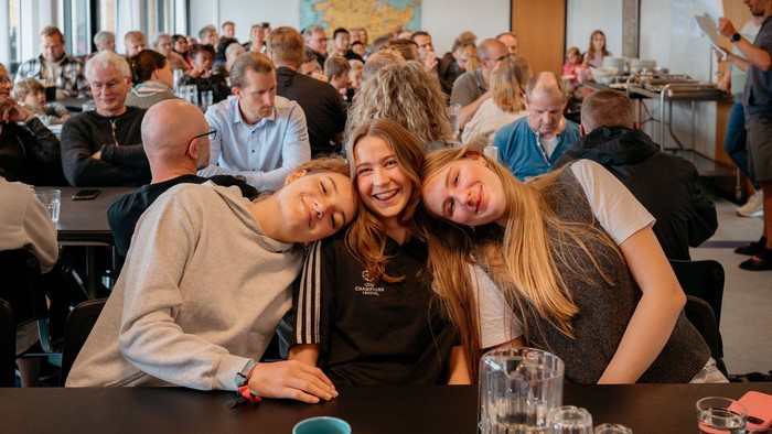 En gruppe venner smiler til kameraet på en fest med mange andre i baggrunden.