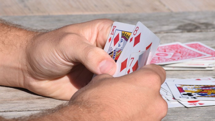 Eine Person hält Karten in der Hand, darunter die Pik-Dame und Pik-Bube.