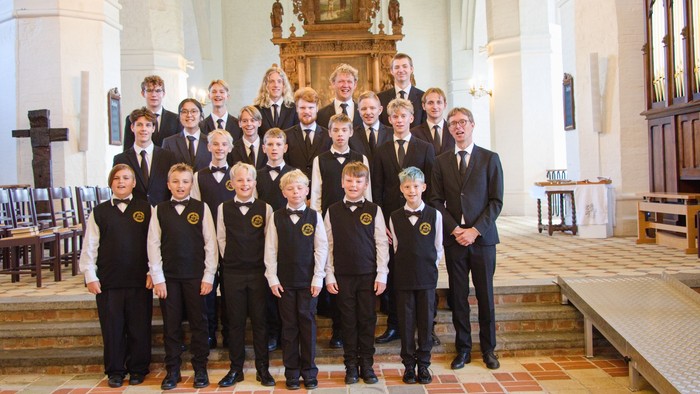 Gruppe af unge mænd i kordragt, der poserer i en kirke.