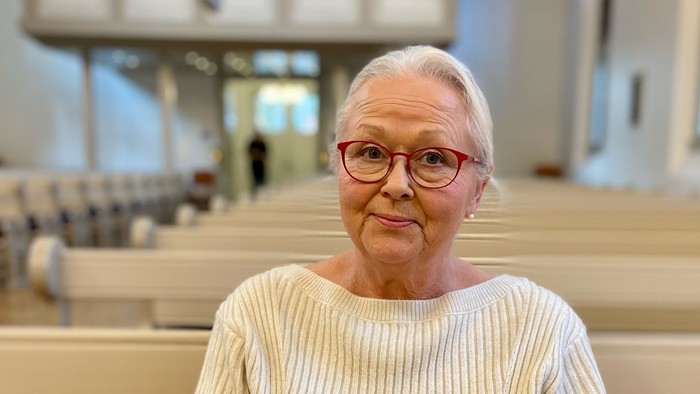 En kvinde står i en kirke med håndene sammen.