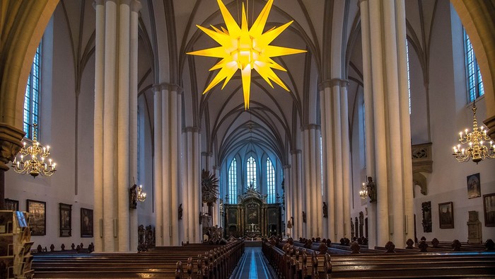 Große Kirche mit hohem, beleuchtetem Stern an der Decke und Reihen von Kirchenbänken.