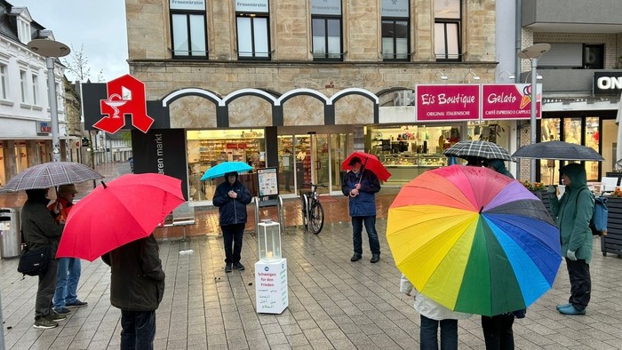 Auf dem Bild sieht man die Gruppe schweigen für den Frieden auf dem oberen Markt in Ibbenbüren. Die Gruppe steht im Kreis, in der Mitte eine Kerze!