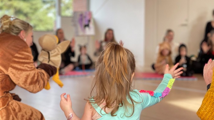 En gruppe børn og voksne sidder på yoga-matser og udfører yoga-øvelser i en lys og rummelig rum.