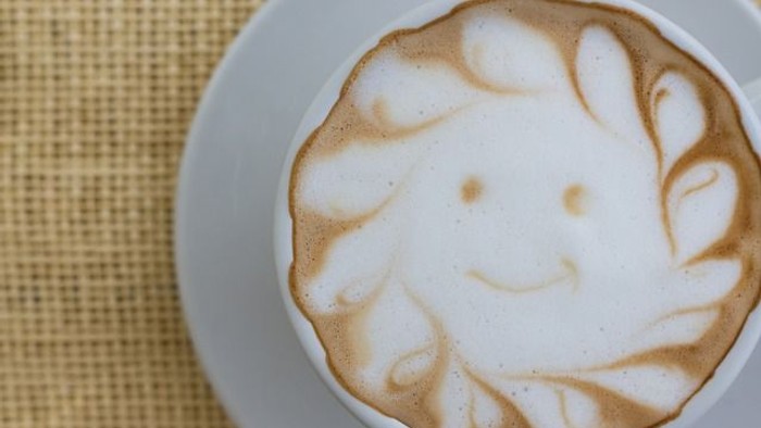 Ein weißer Becher mit Milchschaum und einem Lächeln darauf.