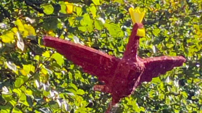 Ein roter Vogel sitzt auf einem Pfahl vor grünem Blattwerk