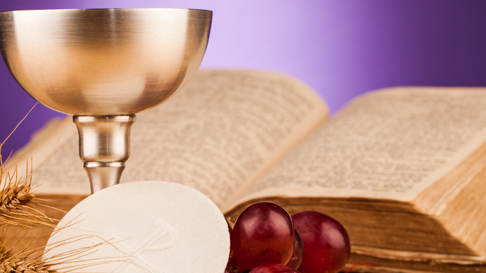 A chalice, bread, and grapes are placed near an open book