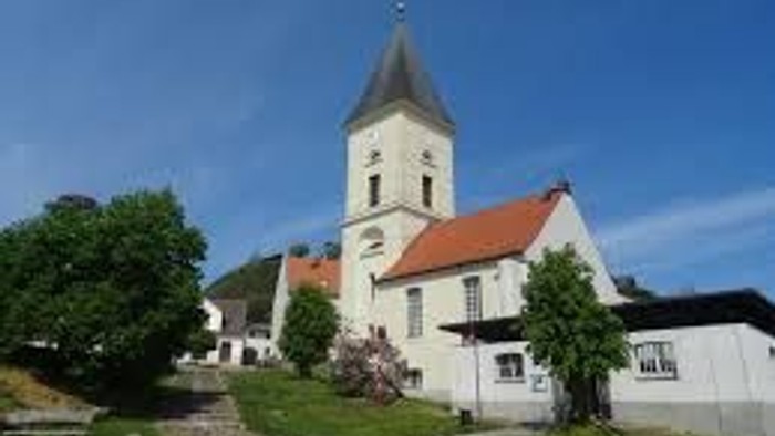 Kleine Kirche mit hohem Turm und rotem Dach in ländlicher Umgebung.