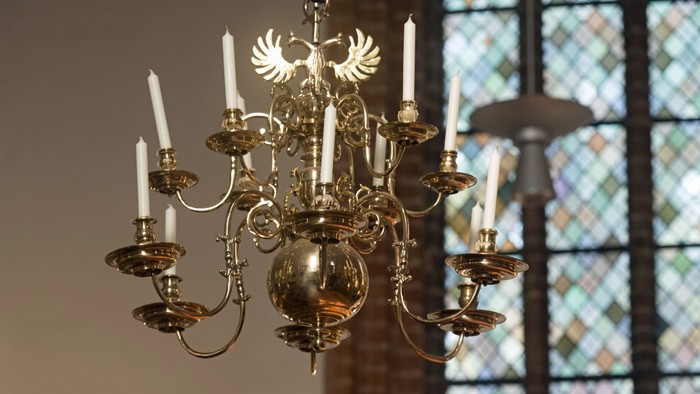 Ein Kronleuchter mit weißen Kerzen vor einem buntglasfenster