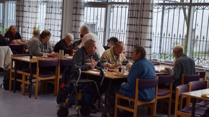 En gruppe ældre personer sidder og spiser sammen i et lys og behageligt indrettet restaurant.