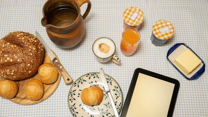 Das Bild zeigt ein Frühstück mit Brot, Butter, Marmelade und Tee.