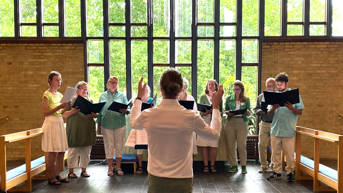 En gruppe af korister optræder i et rum med store vinduer.