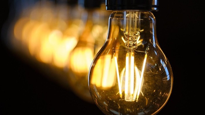 Et nærbillede af en glødende glødepære mod en mørk baggrund med andre pærer i baggrunden.