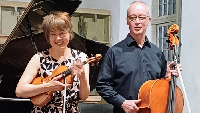 Musiker posieren mit Instrumenten vor einem Klavier.