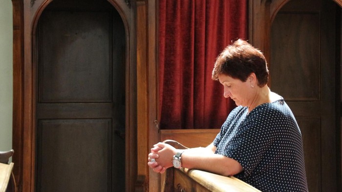 Frau kniet in einer Kirchenbank, die Hände zum Gebet gefaltet.