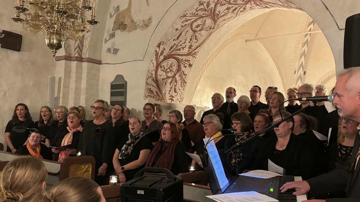 Gruppe af mennesker, der optræder i en prægtig sal med krystalkrone og buedgang.