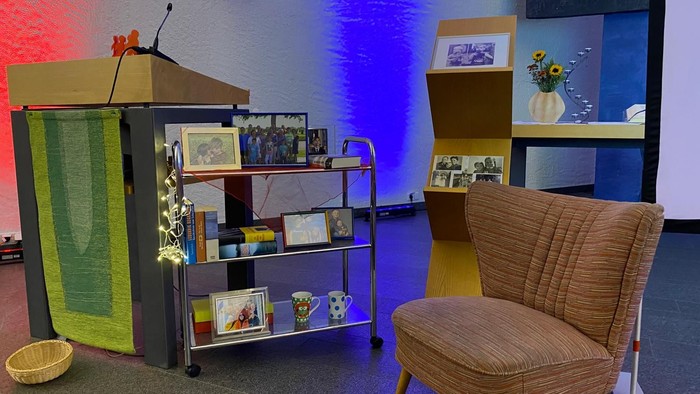 Altarraum der Versöhnungskirche , im Vordergrund ein Sessel, Regale und das Ambo. Im Hintergrund die blau und rot angestrahlte Wand der Kirche und ein Stückchen vom Felger Triptychon.